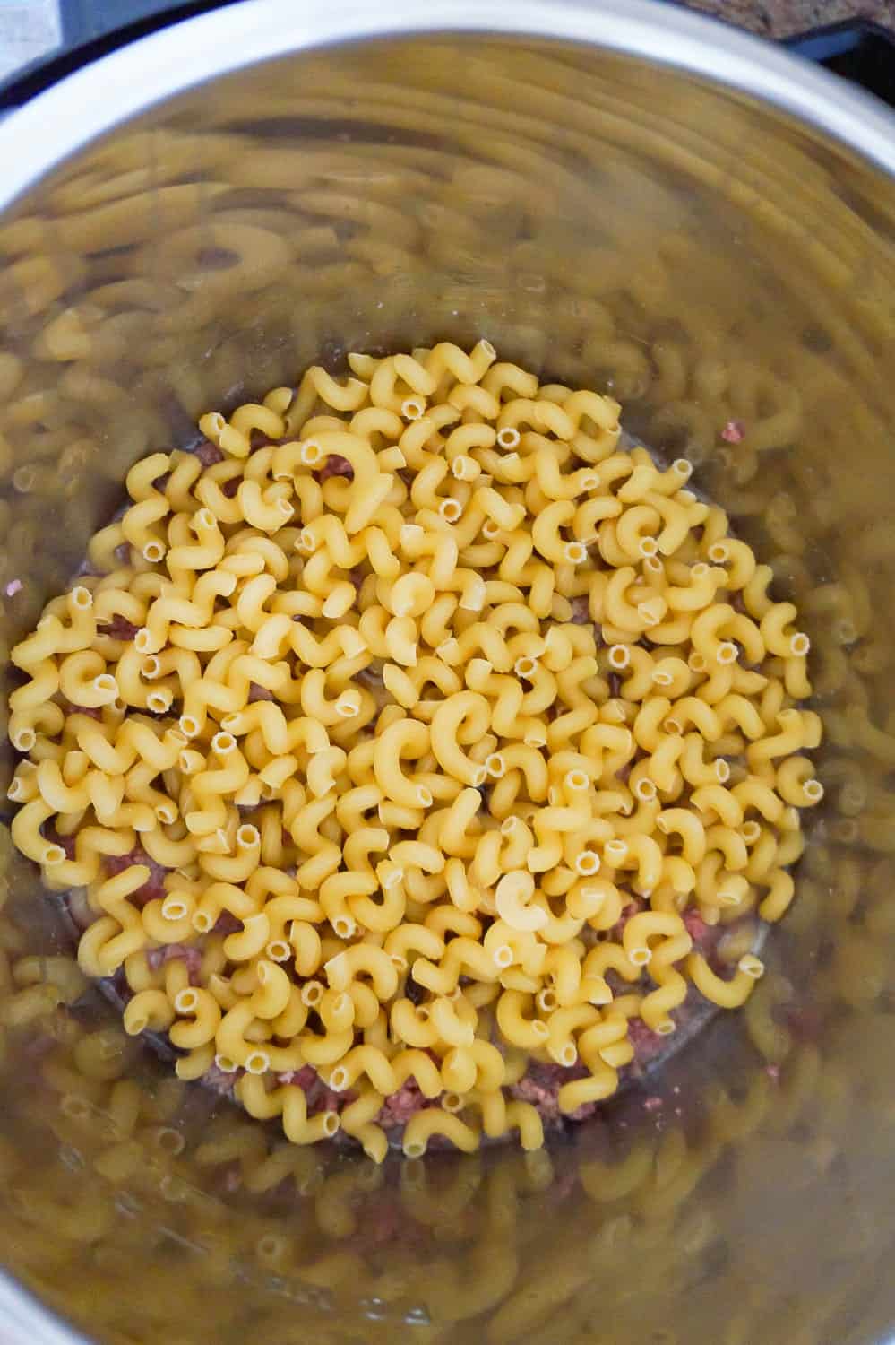 uncooked cavatappi pasta on top of ground beef in an Instant Pot