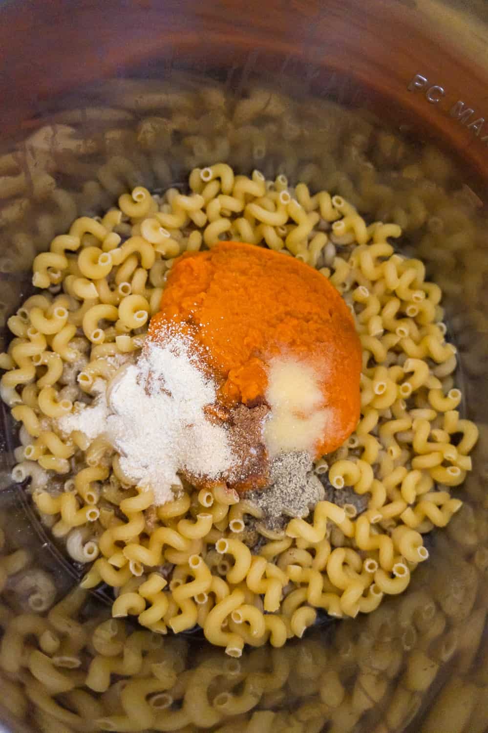 canned pumpkin and spices on top of cavatappi noodles in an Instant Pot before cooking