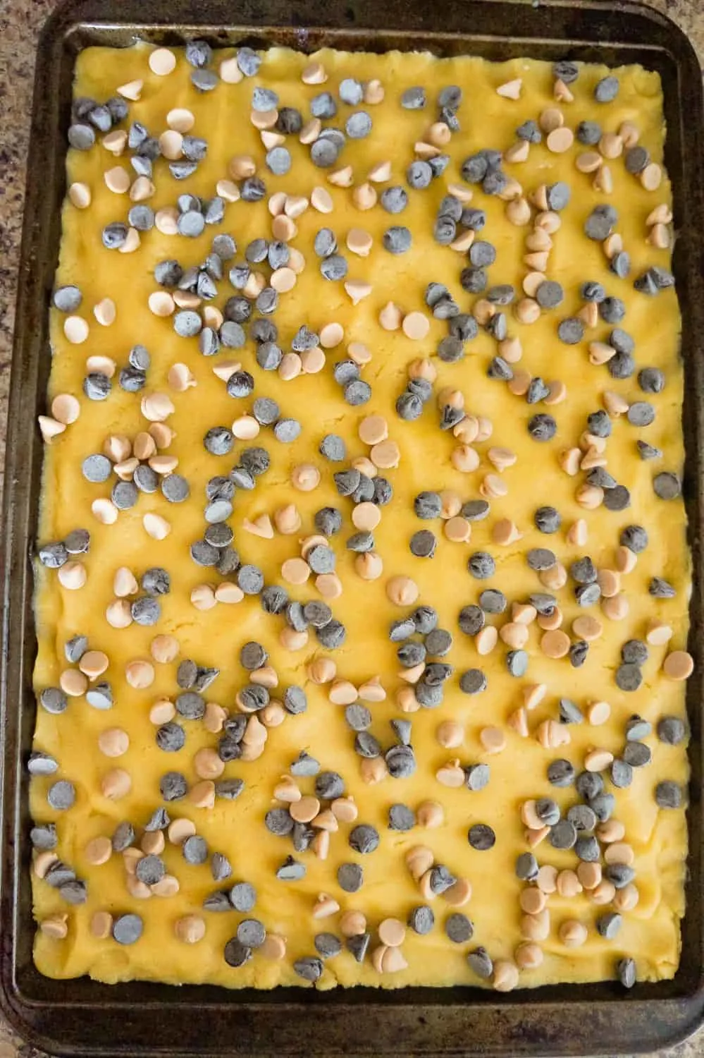 chocolate chips and peanut butter chips on top of banana sugar cookie dough on a baking sheet