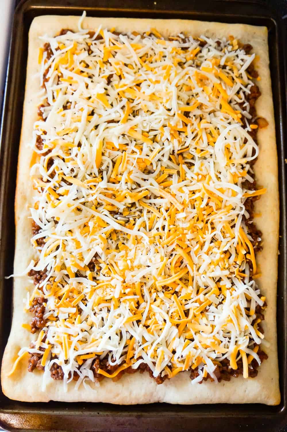shredded mozzarella and cheddar cheese on top of sloppy joe pizza before baking