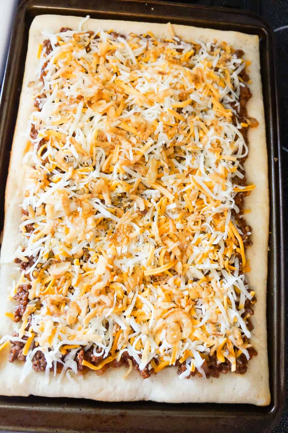 shredded mozzarella cheddar and French's fried onions on top of sloppy joe pizza before baking