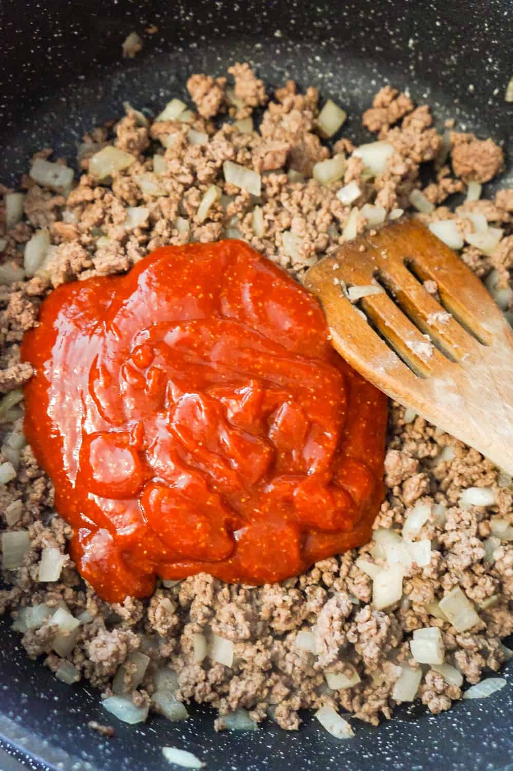 sloppy joe sauce on top of cooked ground beef and diced onions in a saute pan