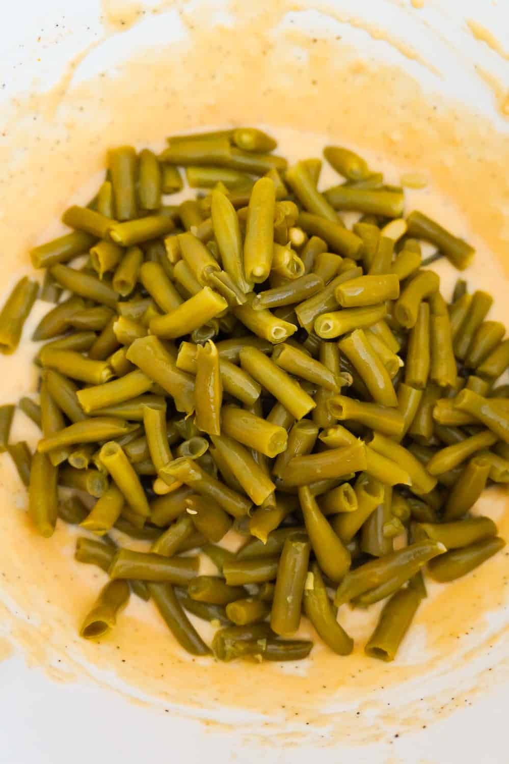 canned cut green beans on top of cheese soup mixture in a mixing bowl