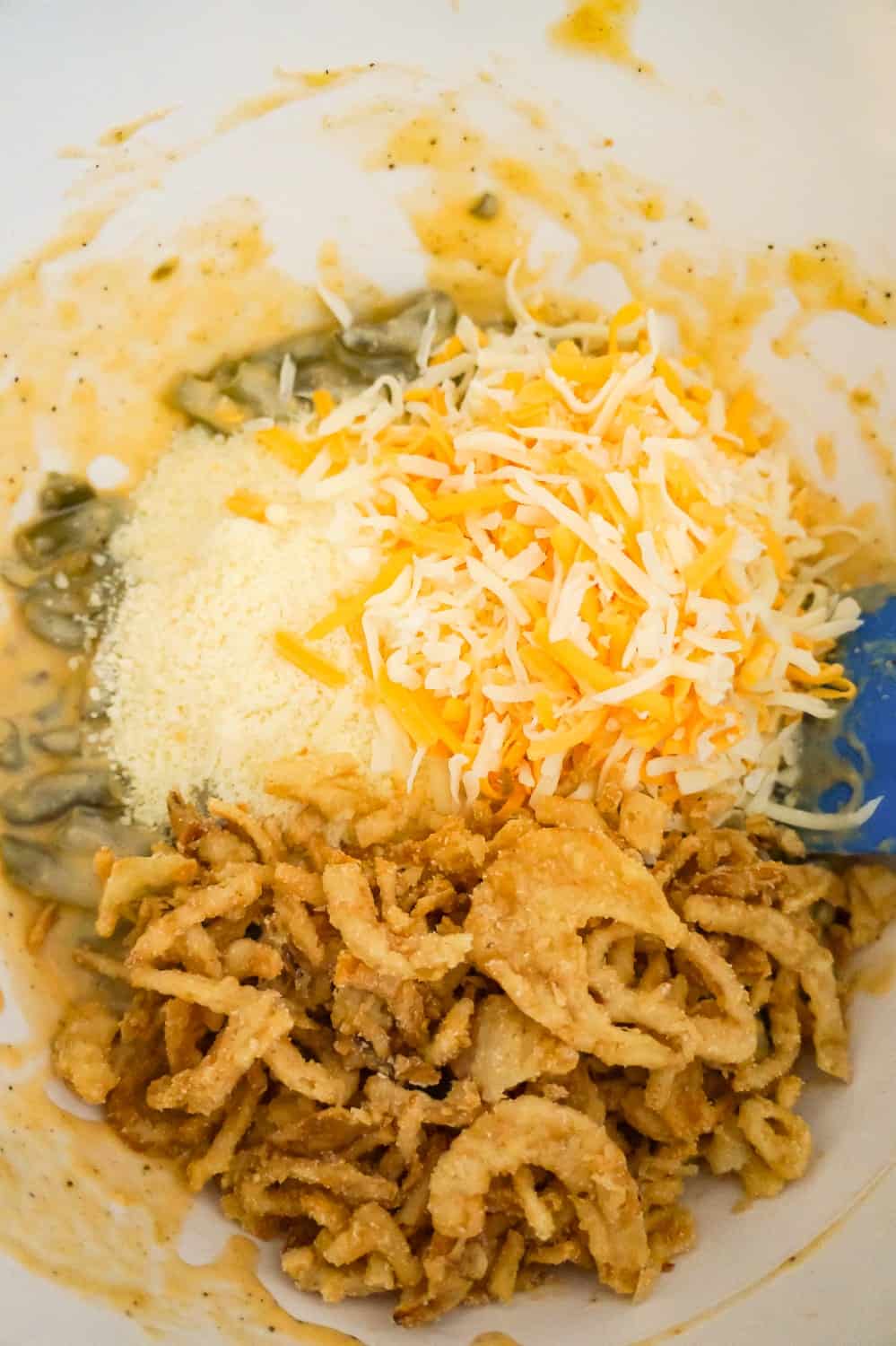 shredded Parmesan, mozzarella, cheddar and French's fried onions on top of green bean mixture in a mixing bowl