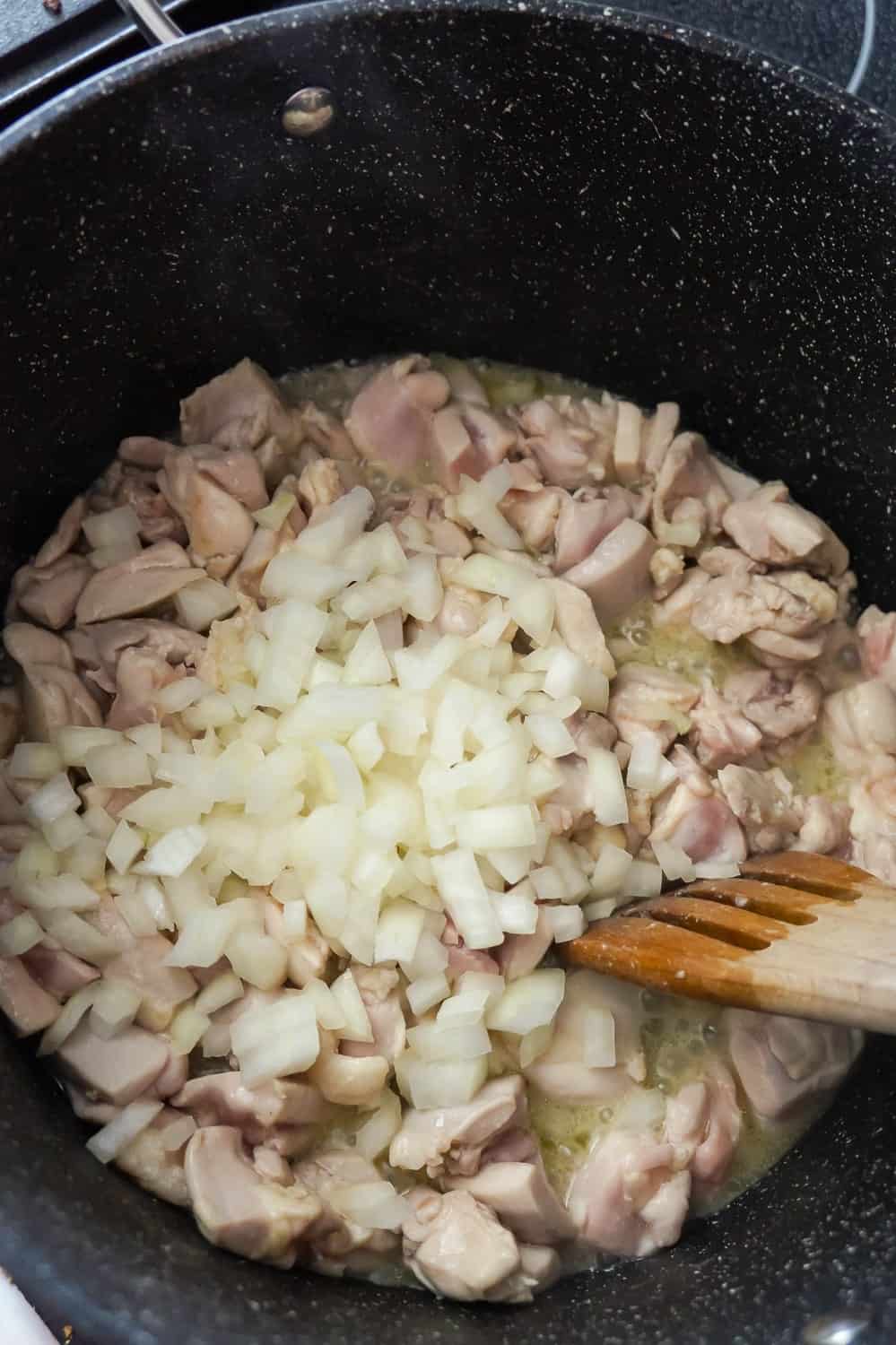 diced onions on top of chicken thigh pieces in a large pot