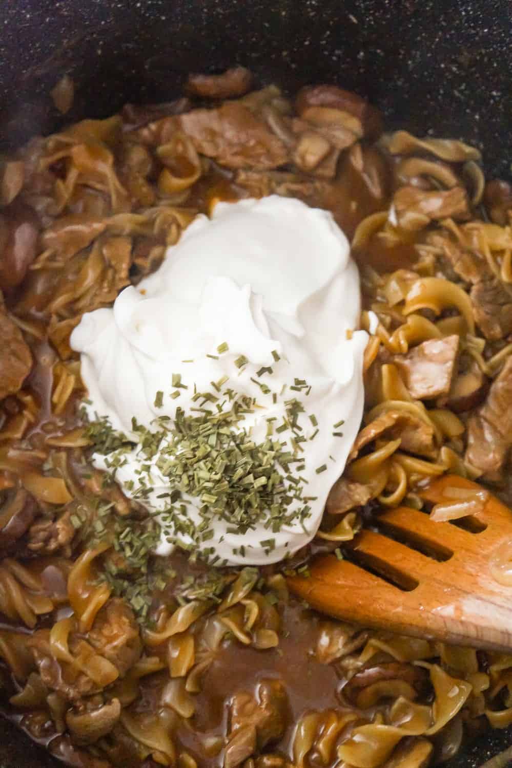 sour cream and dried chives on top of steak and noodles in a large pan
