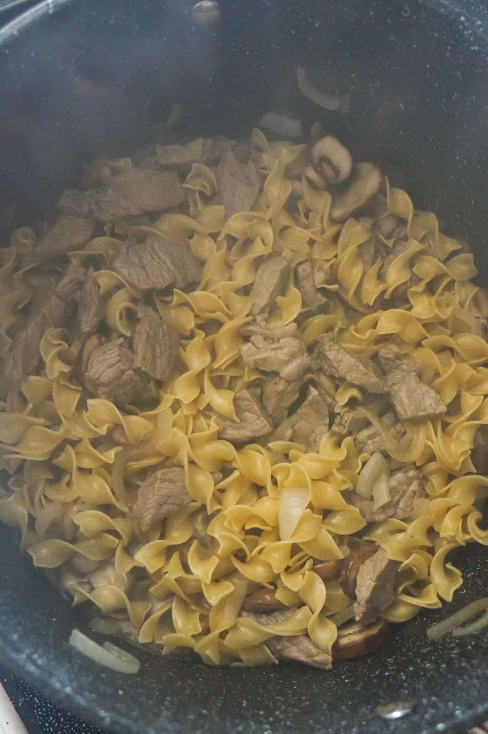 steak pieces and egg noodles in a large pan