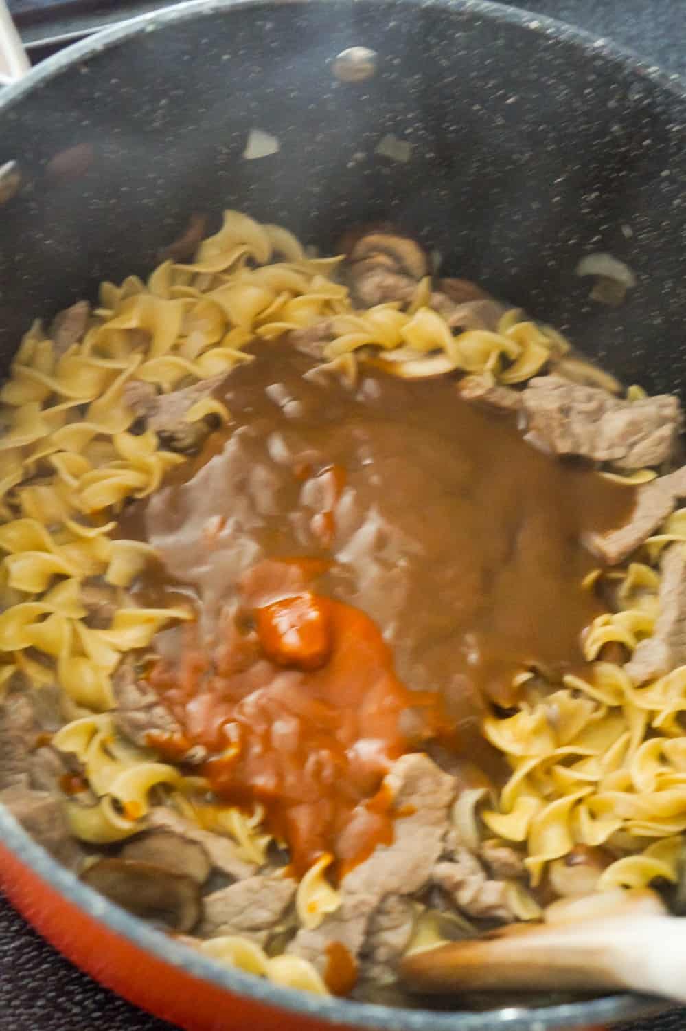 gravy and Heinz 57 sauce on top of egg noodles and steak pieces in a large pan
