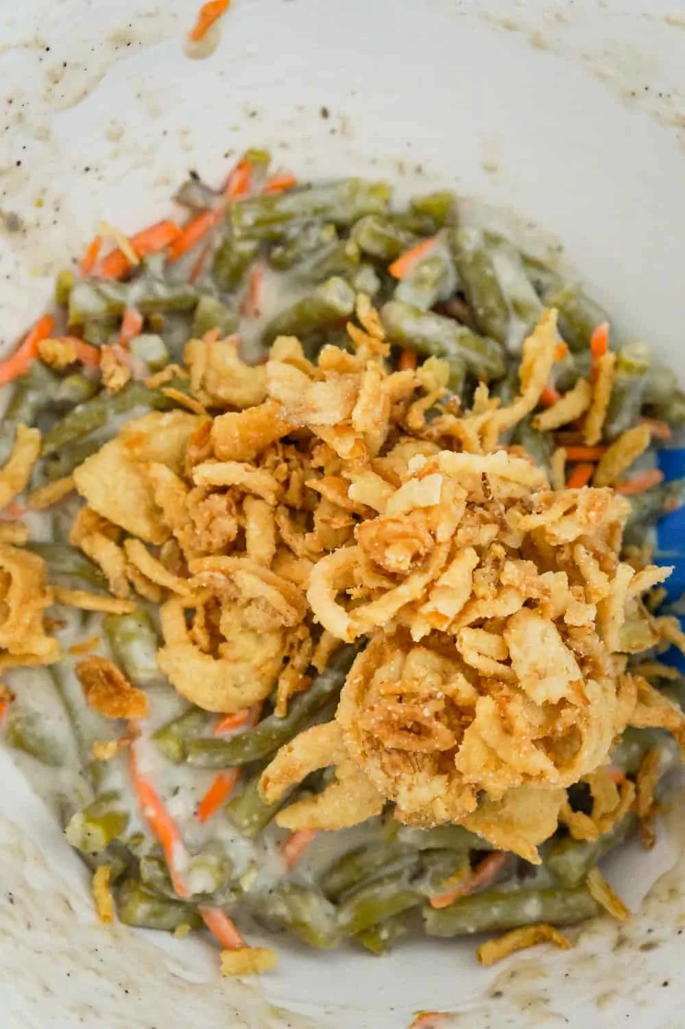 French's fried onions on top of green bean and carrot mixture in a mixing bowl