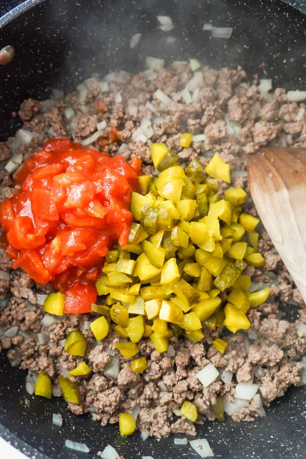 diced pickles and diced tomatoes on topped of cooked ground beef in a saute pan