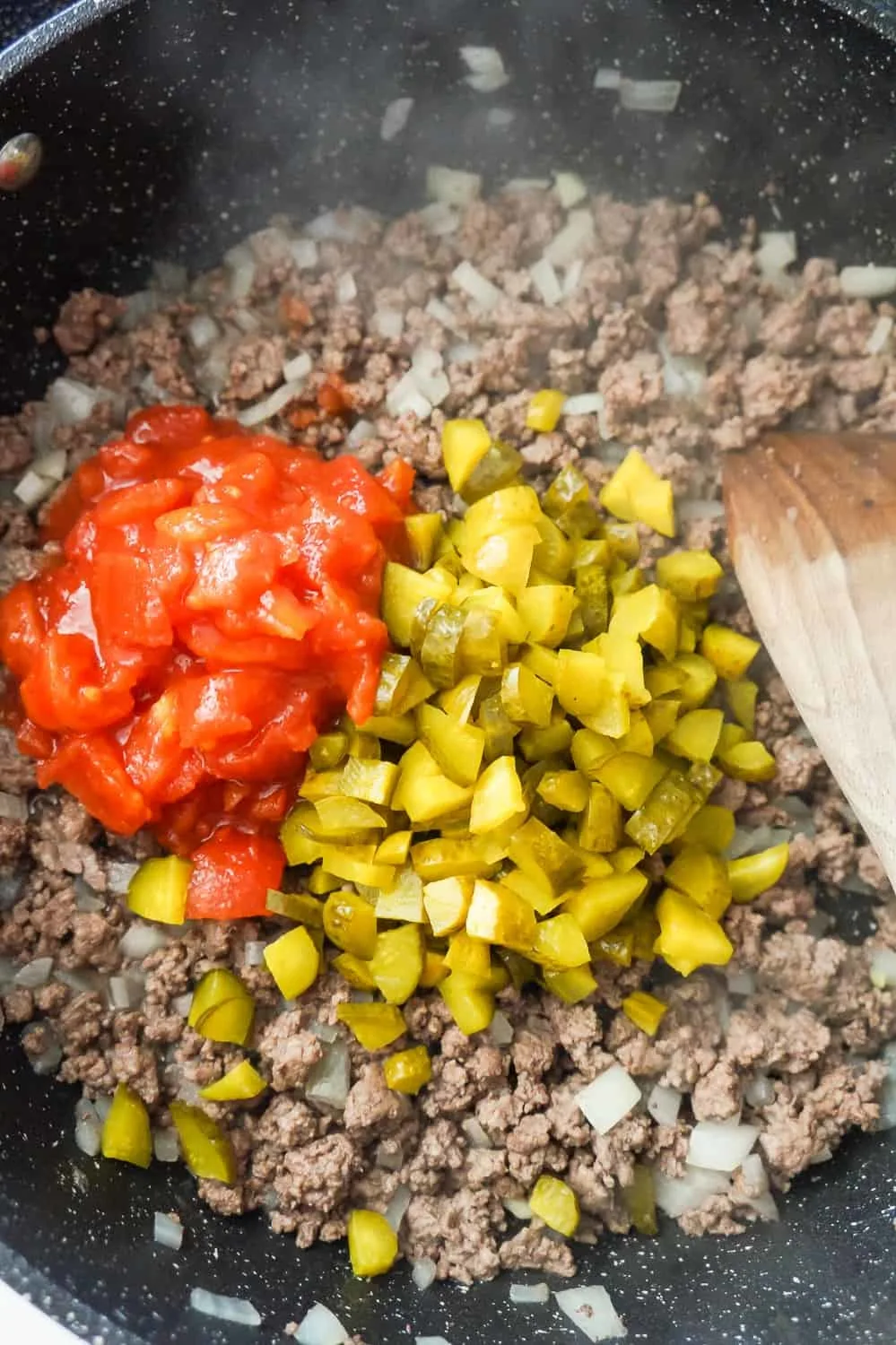 diced pickles and diced tomatoes on topped of cooked ground beef in a saute pan
