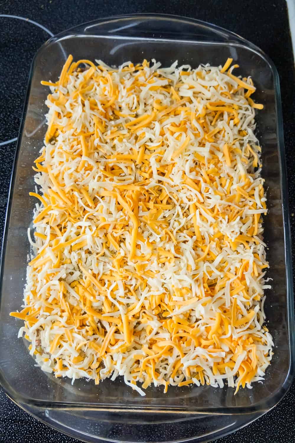 shredded cheddar and mozzarella on top of ground beef casserole in a baking dish