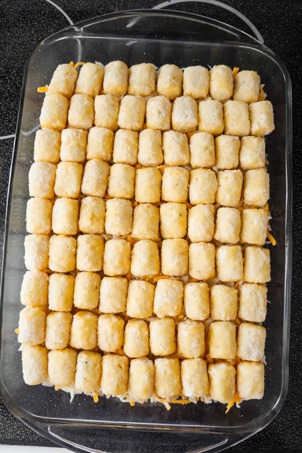 frozen tater tots in a single layer on top of hamburger casserole in a baking dish