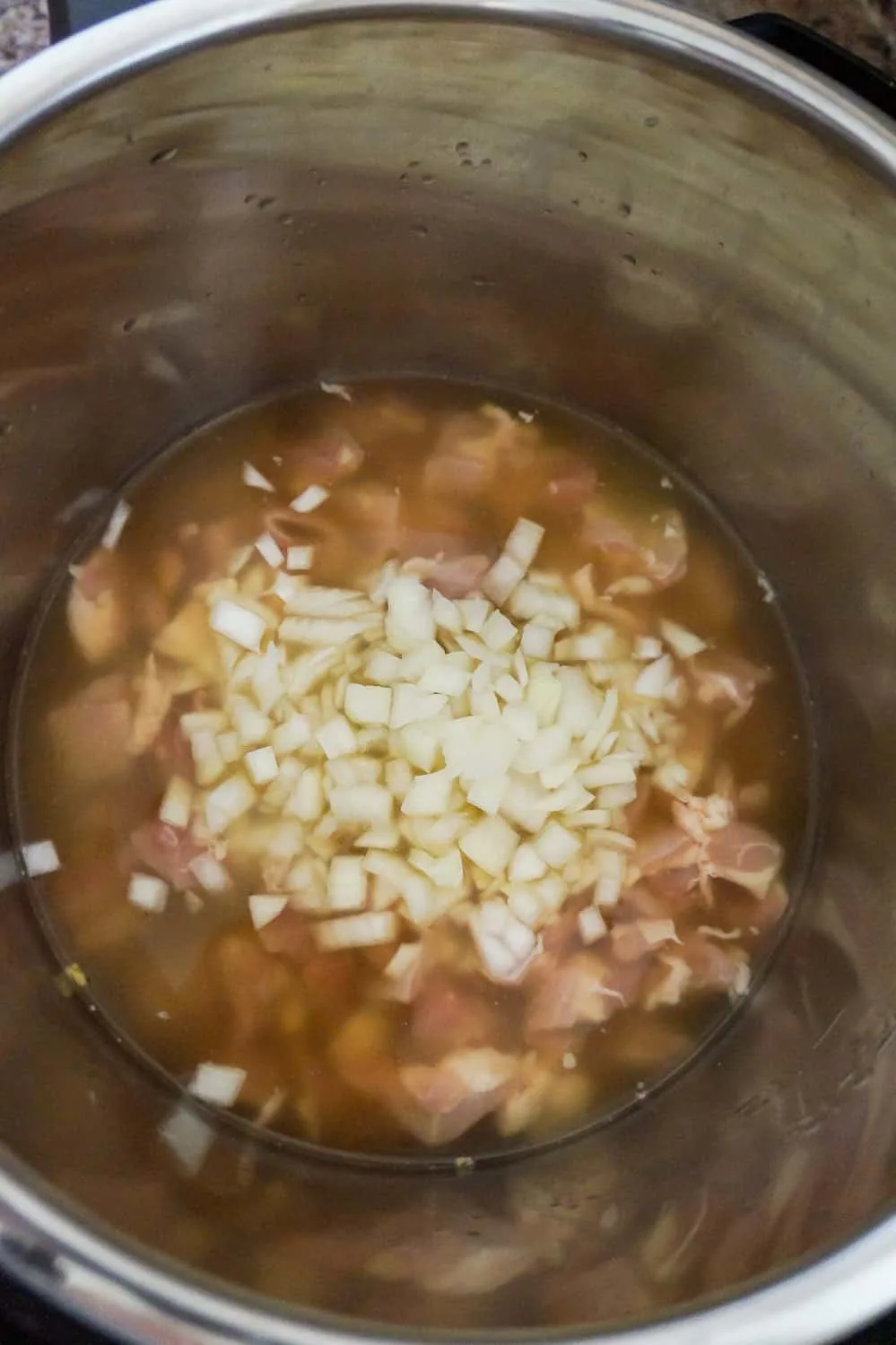diced onions and chunks of chicken in chicken broth in an Instant Pot