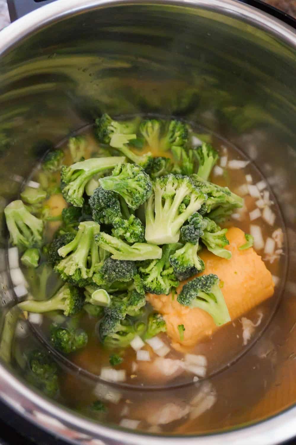 broccoli florets on top of cheese soup and chunks of chicken in an Instant Pot