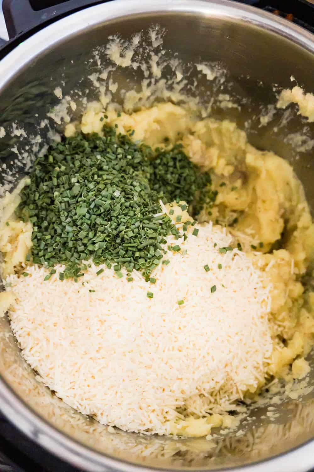 grated Parmesan cheese and chopped chives on top of mashed potatoes in an Instant Pot