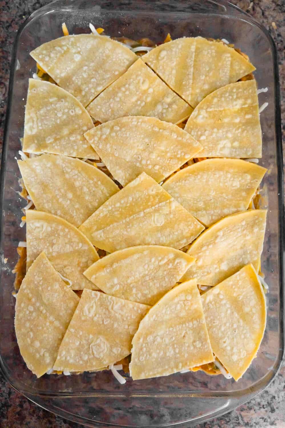 corn tortilla quarters on top of chicken mixture in a baking dish