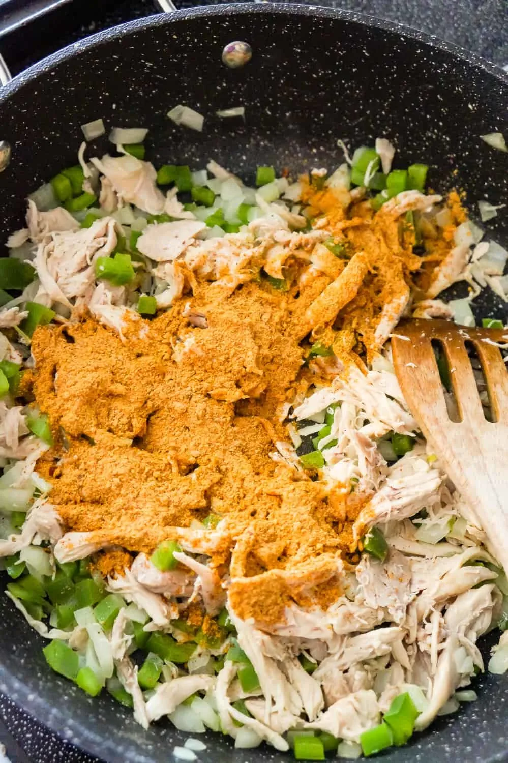 chicken taco seasoning on top of shredded chicken, diced onions and diced green peppers in a saute pan