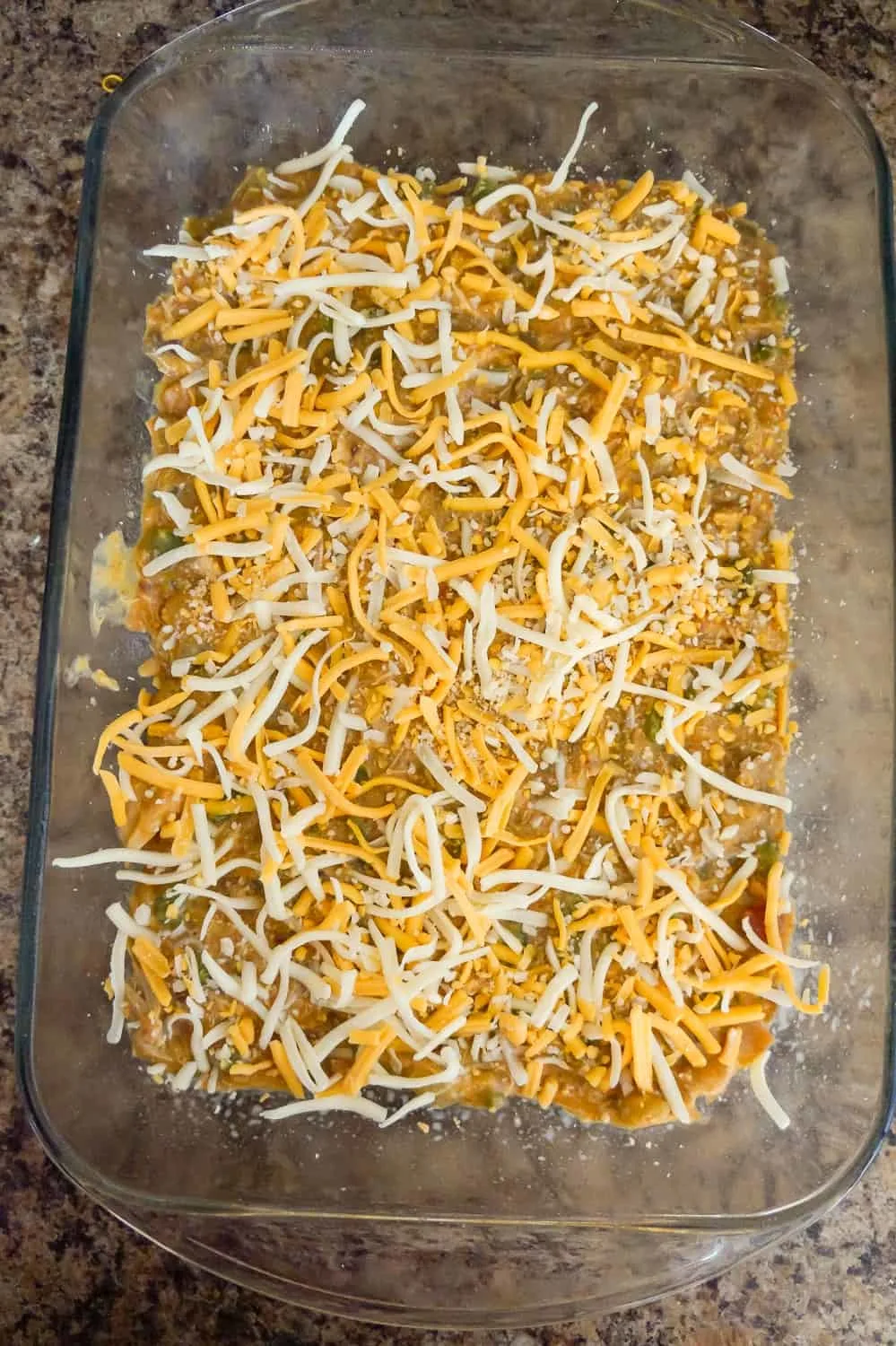 shredded cheese on top of creamy chicken mixture in a baking dish