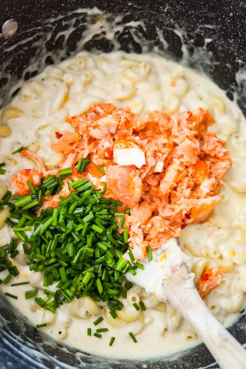 chunks of lobster meat and chopped chives on top of macaroni and cheese in a large pot