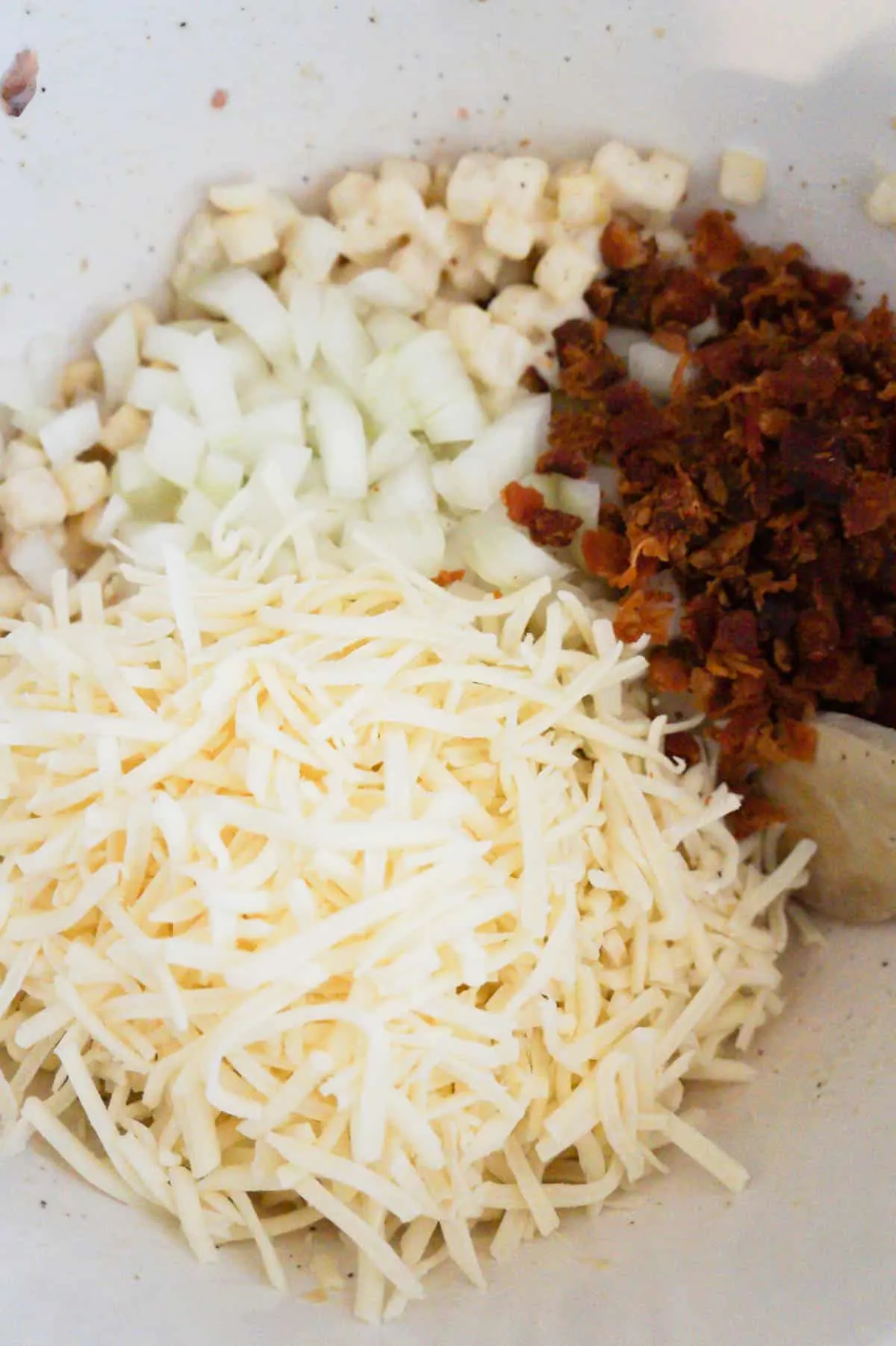 shredded mozzarella cheese, crumbled bacon and diced onions in a mixing bowl