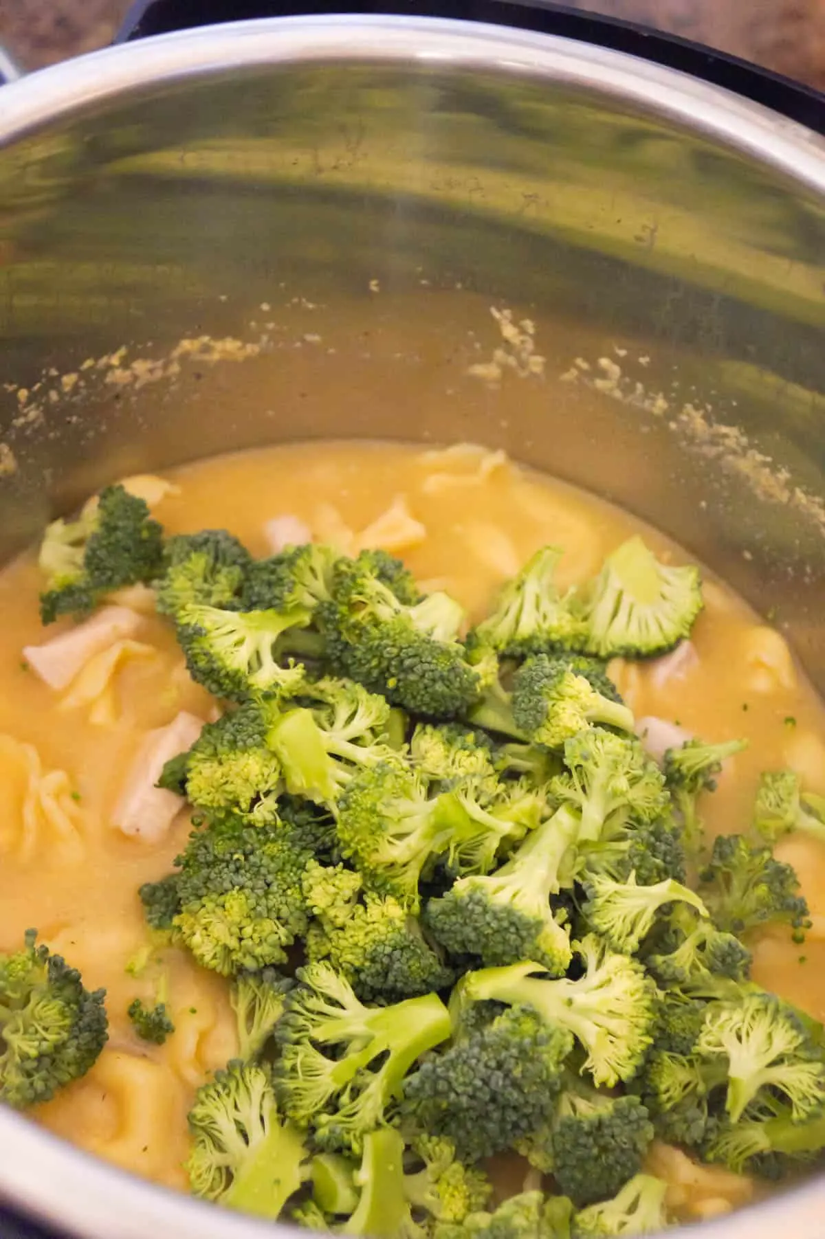 chopped broccoli florets on top of creamy tortellini in an Instant Pot