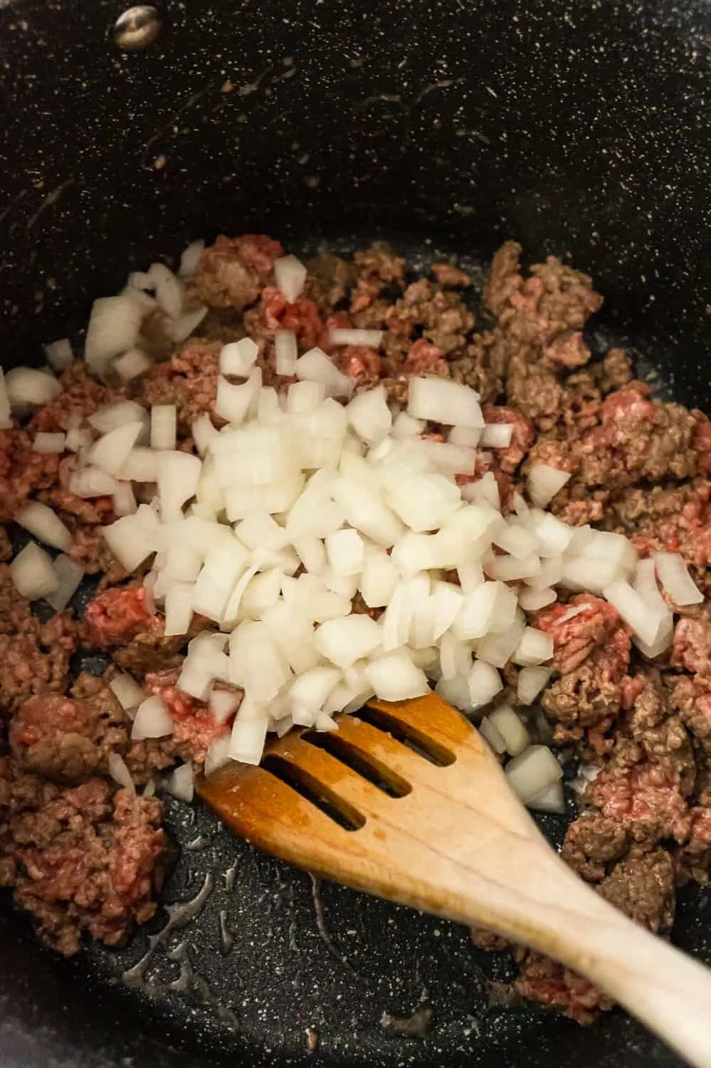 diced onions on top of ground beef in a large pot