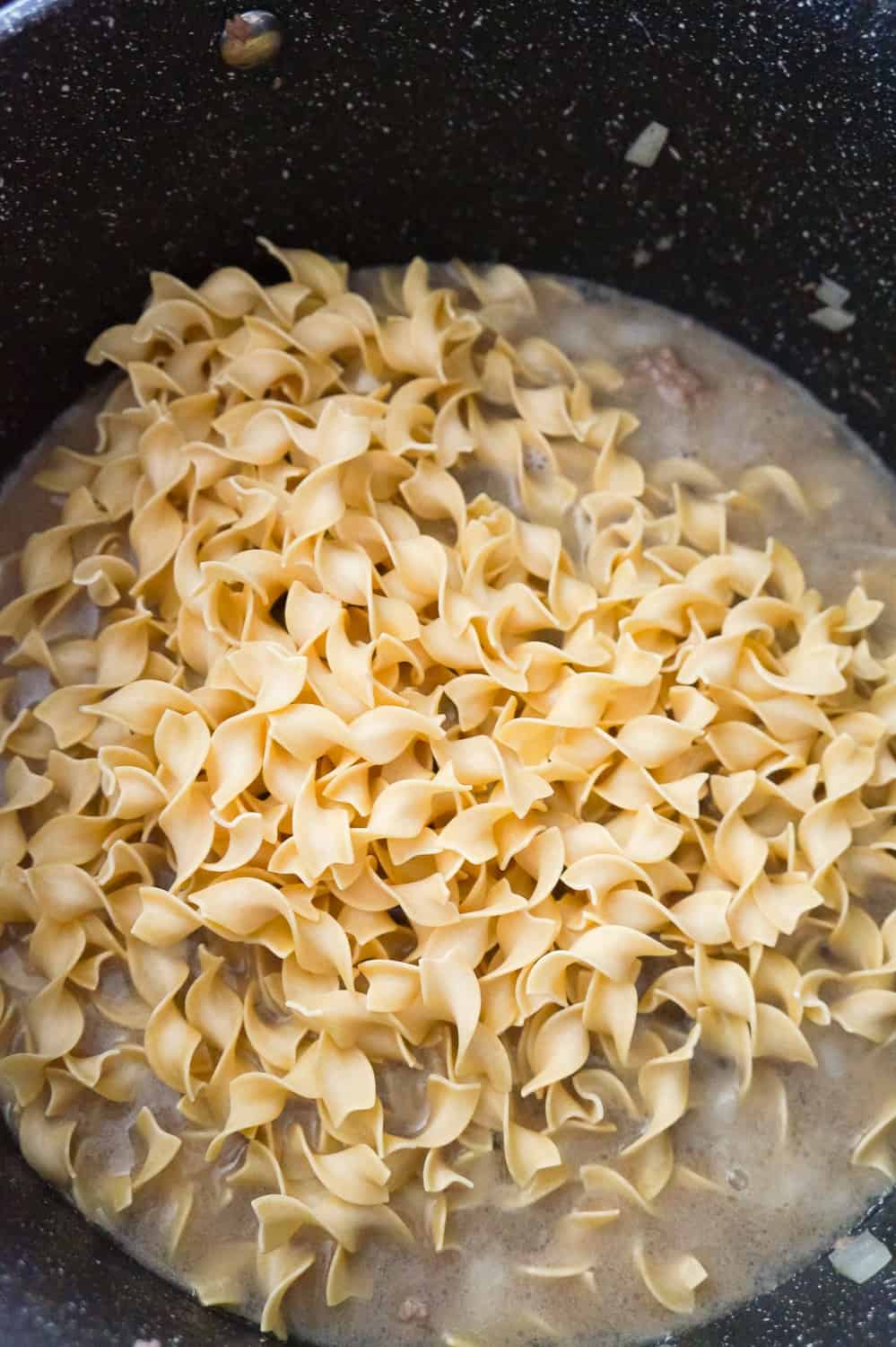 uncooked egg noodles on top of ground beef and water in a pot