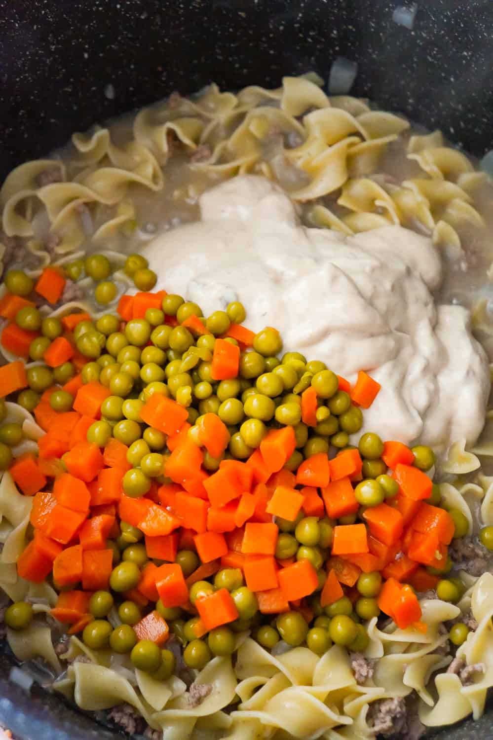 canned peas and carrots and condensed cream of mushroom soup on top of beef and noodles in a pot
