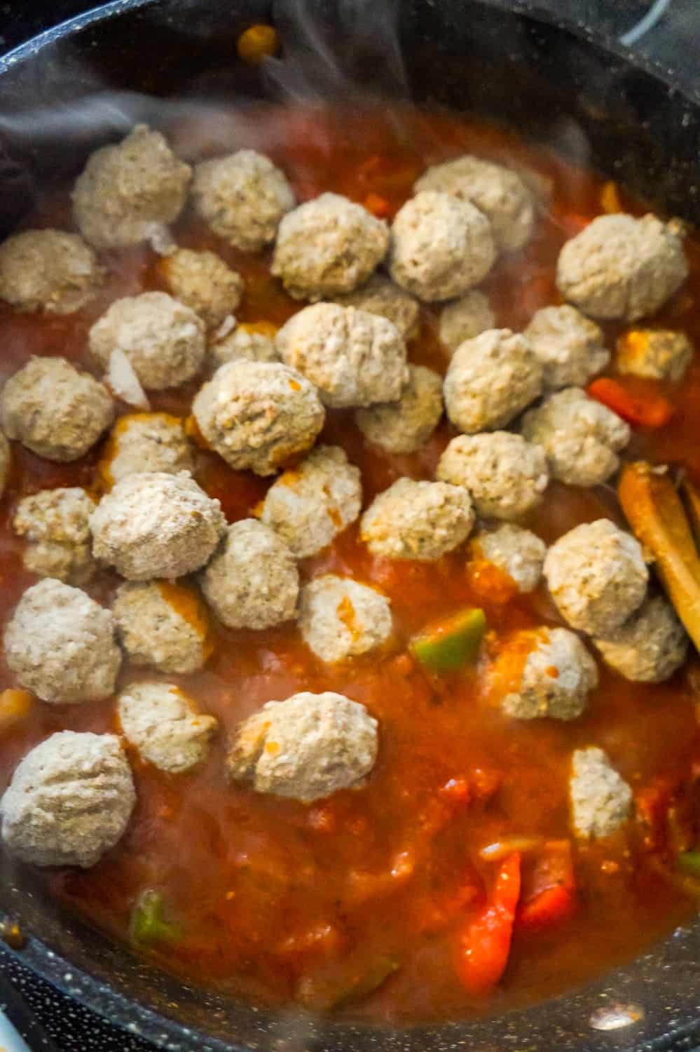 frozen meatballs on top of marinara and chopped bell peppers in a saute pan