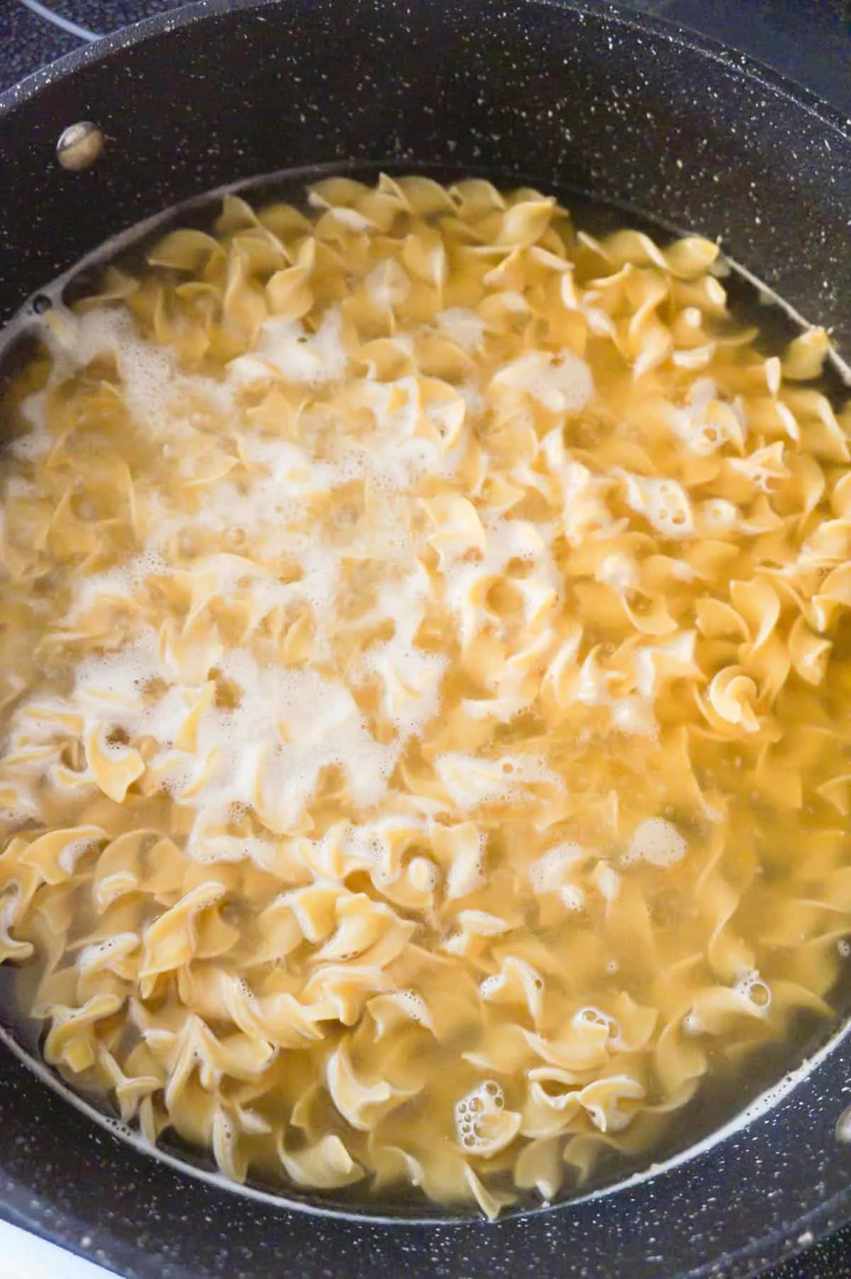 uncooked egg noodles in chicken broth in a pot