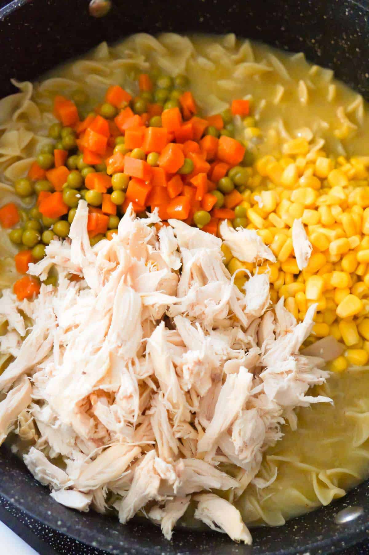 shredded rotisserie chicken, peas and carrots and corn on top of egg noodles in a pot