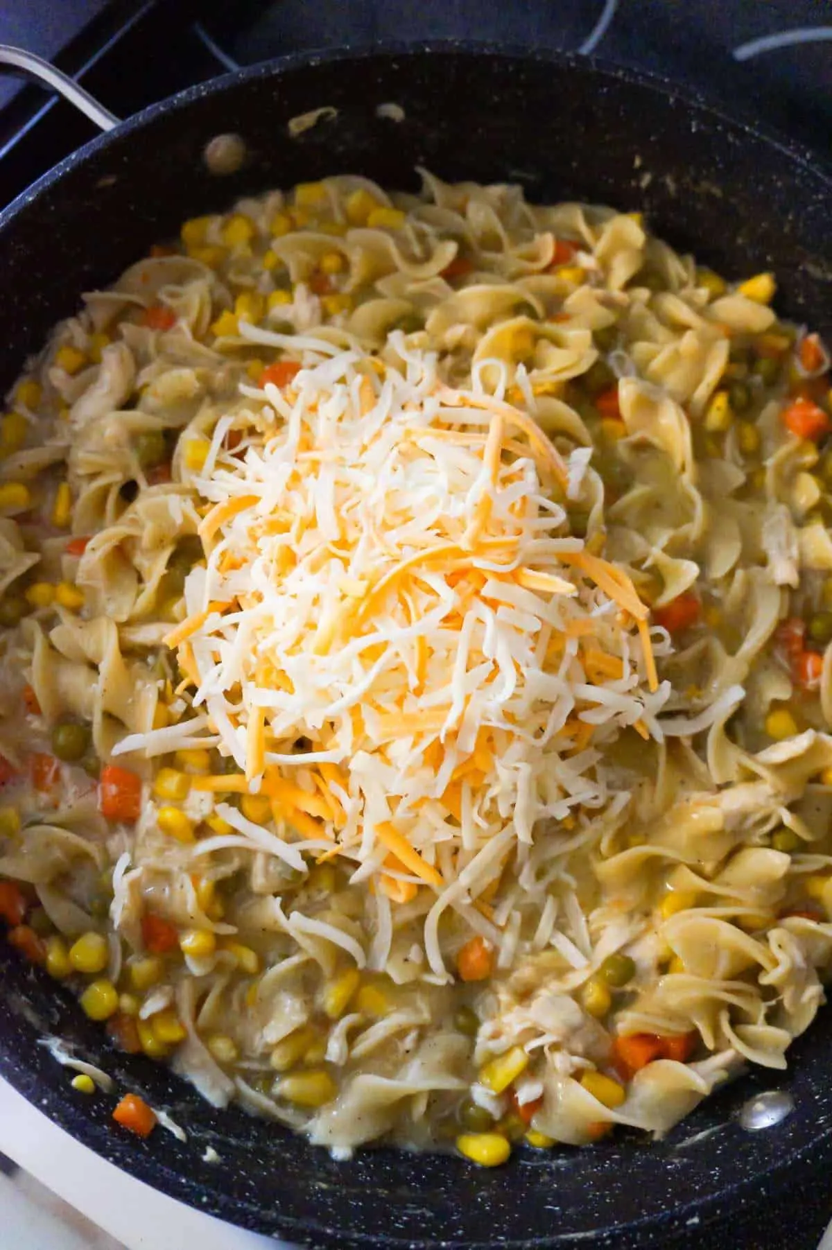 shredded mozzarella and cheddar cheese on top of creamy egg noodles in a pot