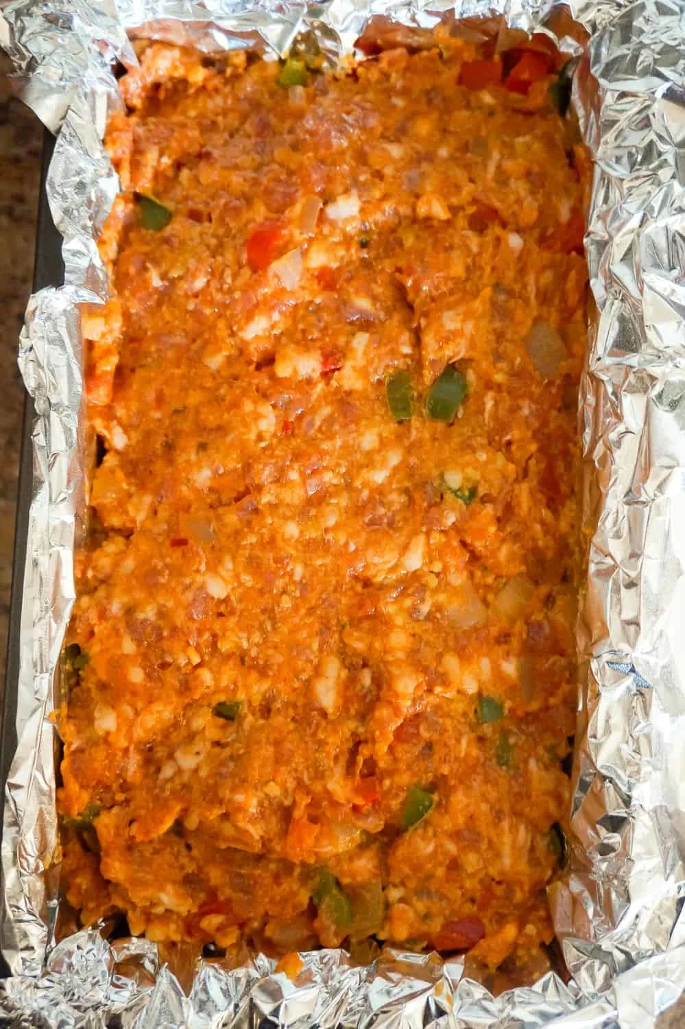 sausage and peppers meatloaf mixture pressed into a loaf pan before baking