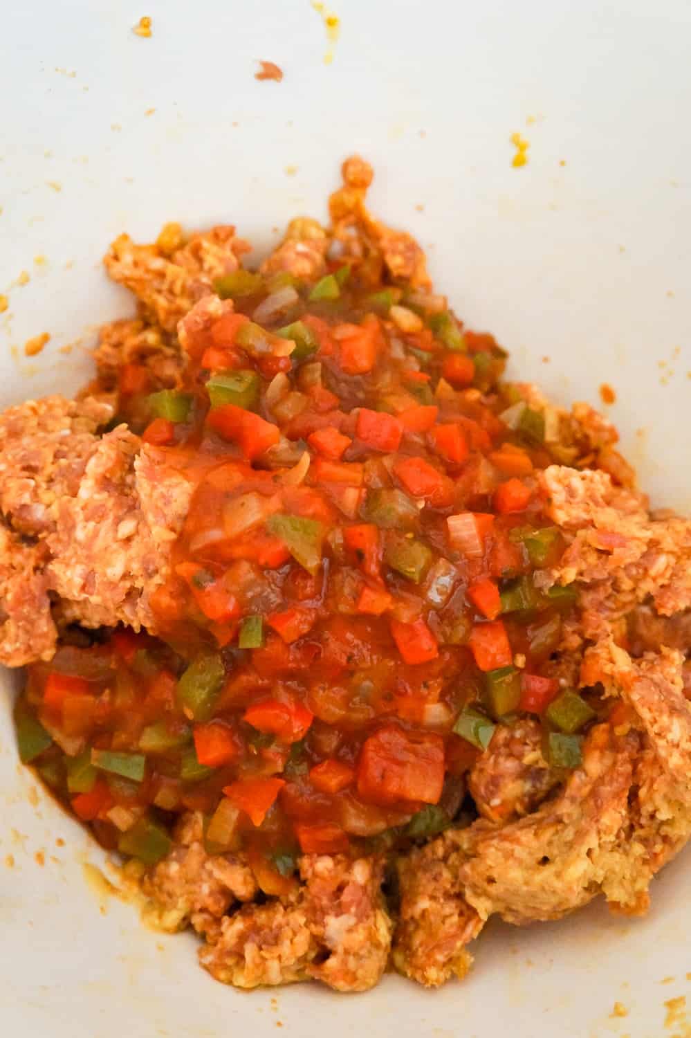 marinara sauce and diced peppers on top of sausage meat in a mixing bowl