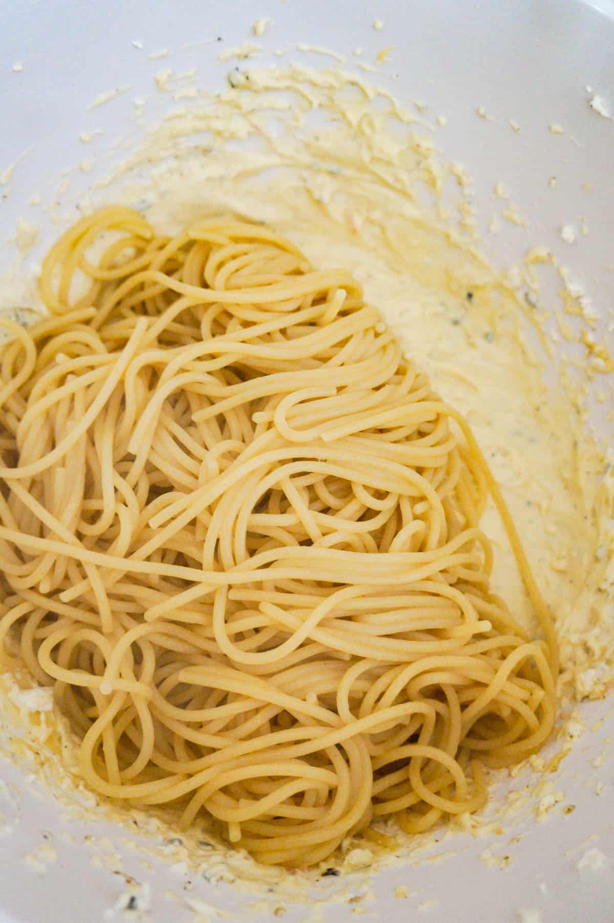 cooked spaghetti on top of cream cheese and cream of chicken soup mixture in a mixing bowl