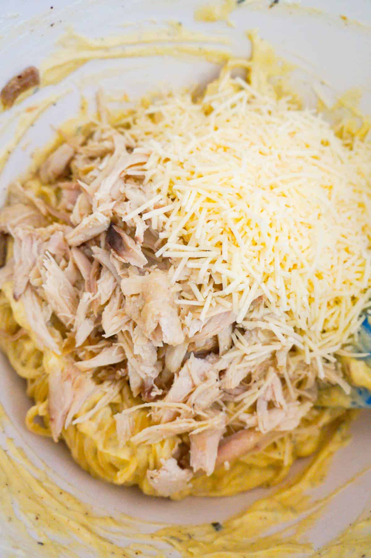shredded Parmesan cheese and shredded turkey on top of creamy spaghetti in a mixing bowl