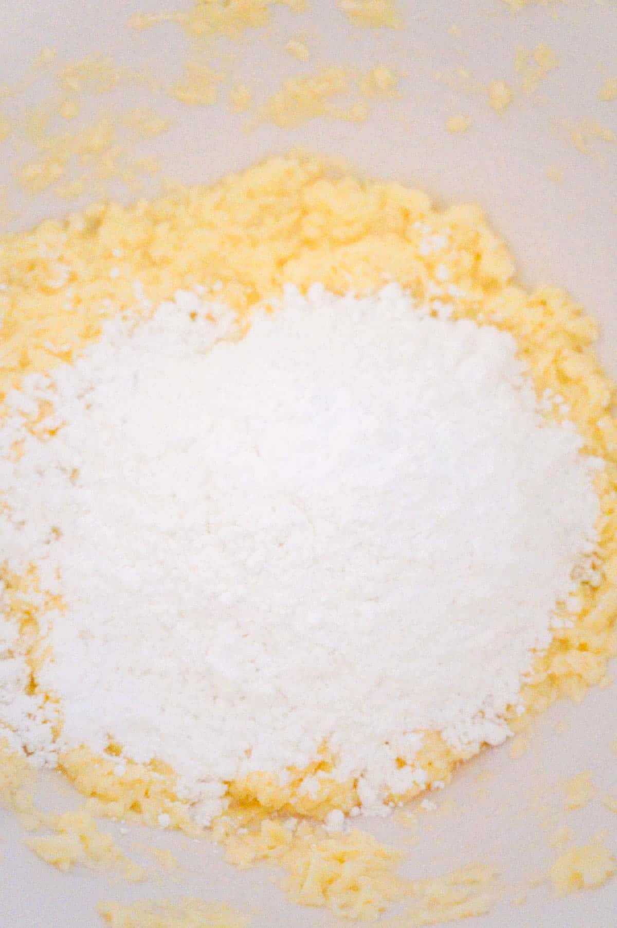 icing sugar on top of butter and egg white mixture in a mixing bowl