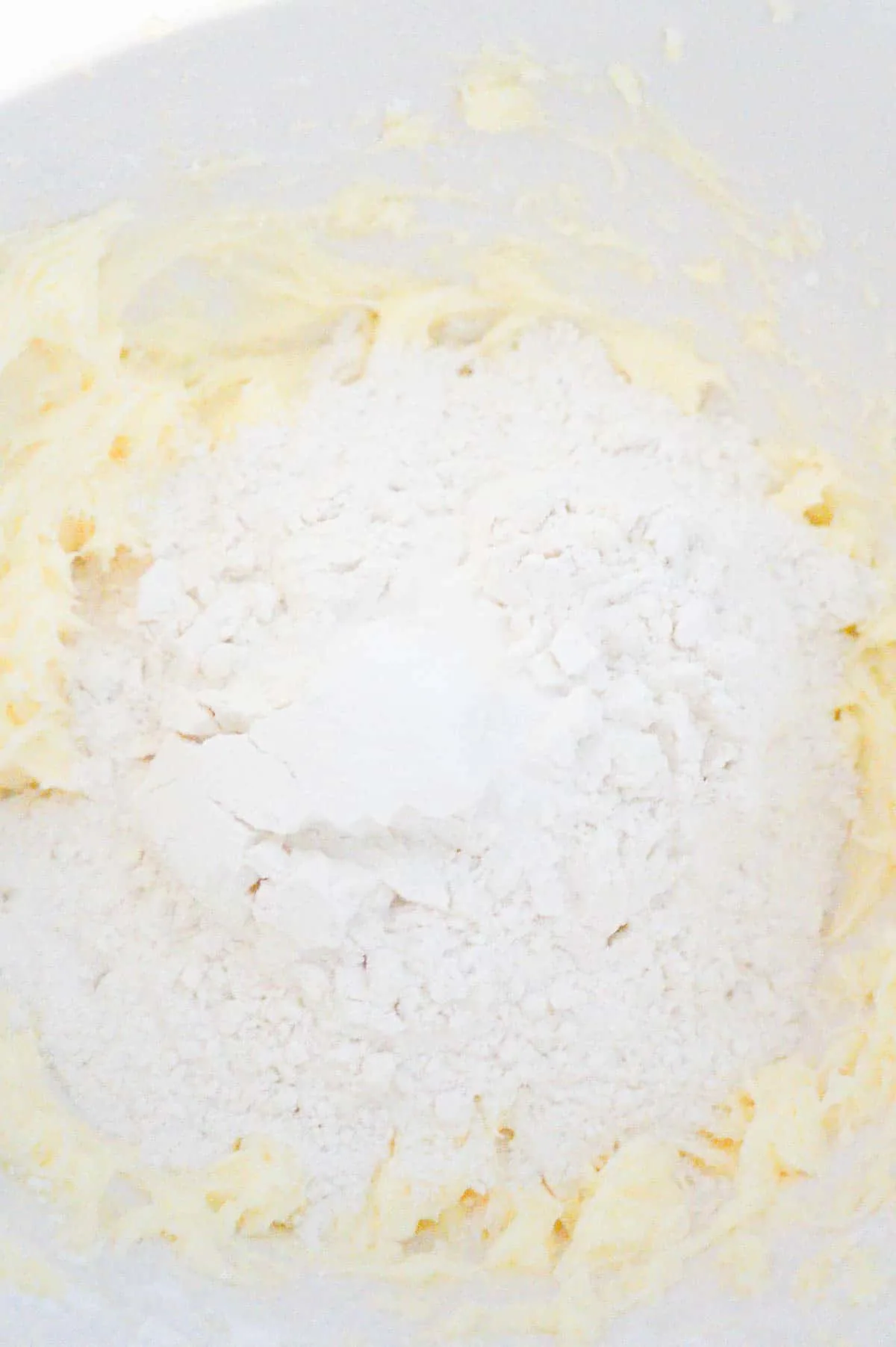 all purpose flour on top of icing sugar and butter mixture in a mixing bowl