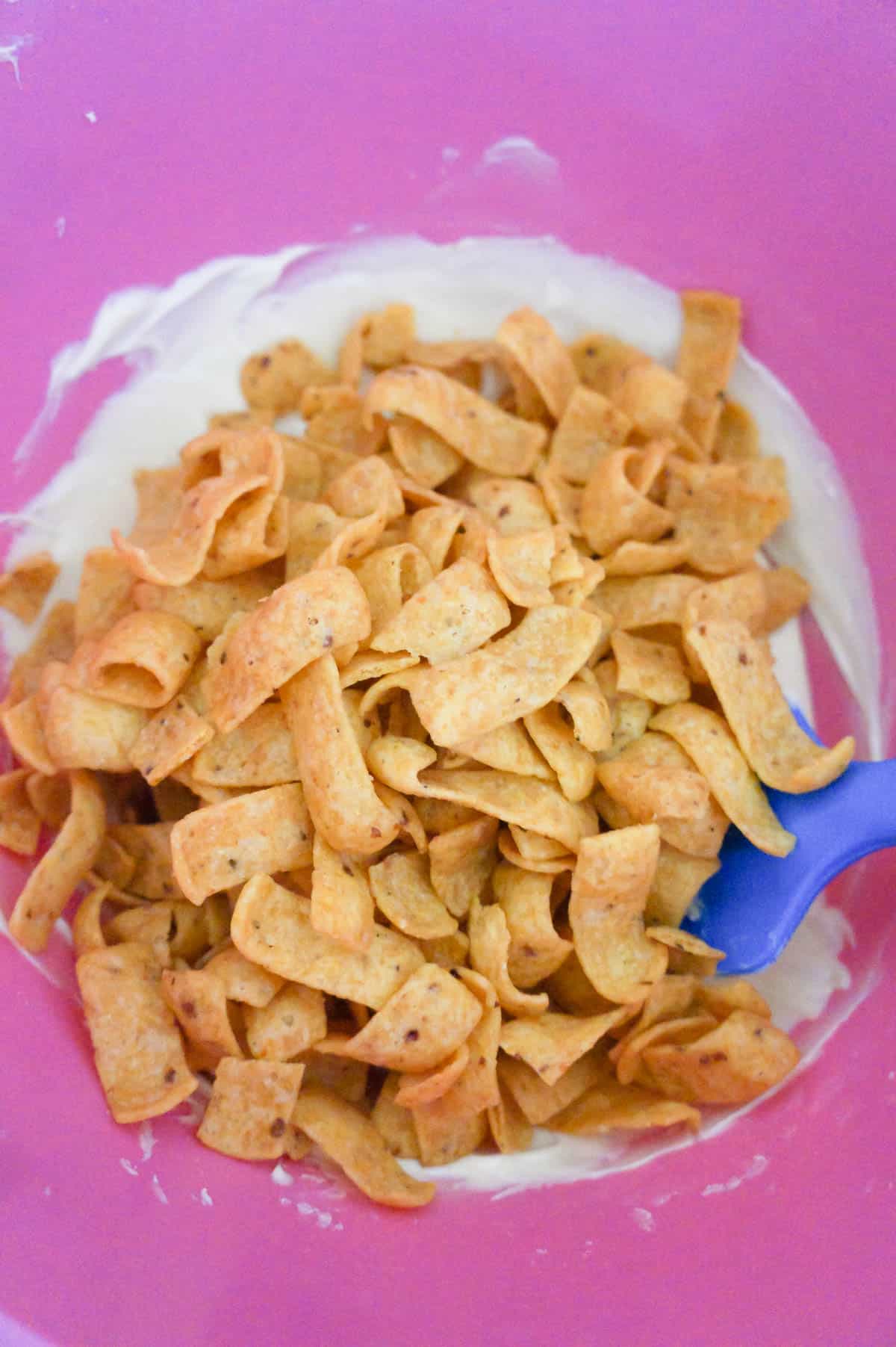 fritos corn chips on top of melted white chocolate in a mixing bowl