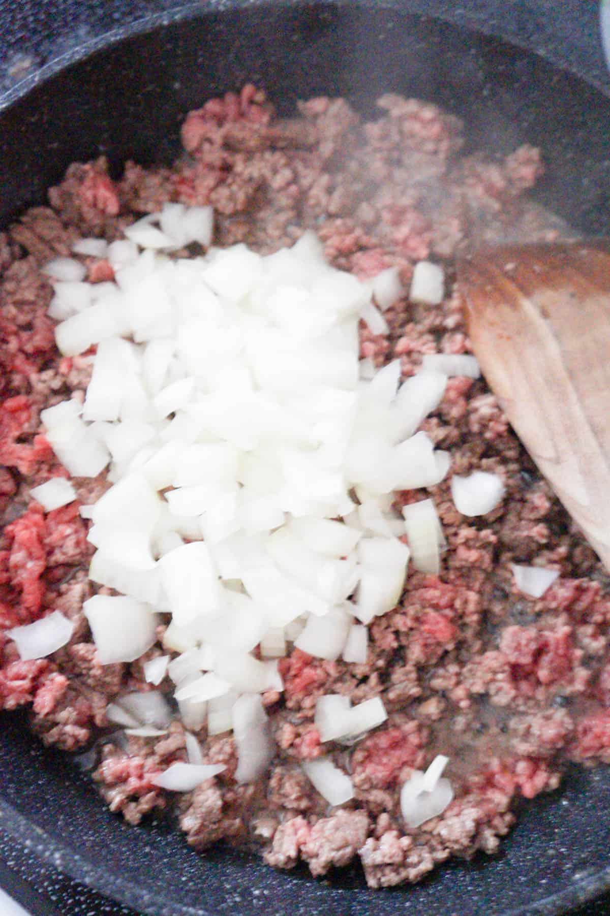 diced onion on top of ground beef cooking in a saute pan