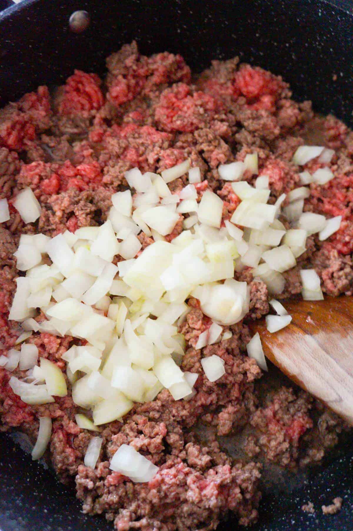 diced onions on top of ground beef cooking in a saute pan