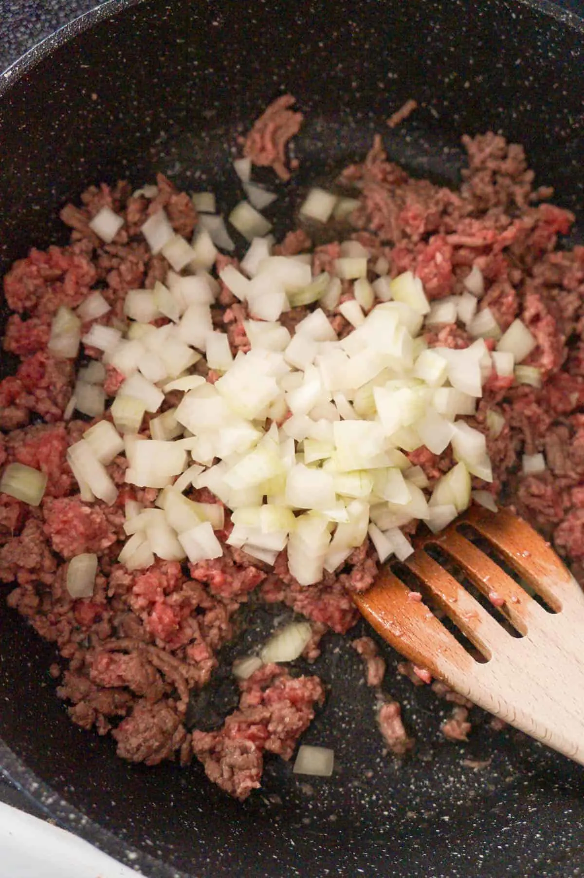 ground beef and diced onions cooking in a saute pan
