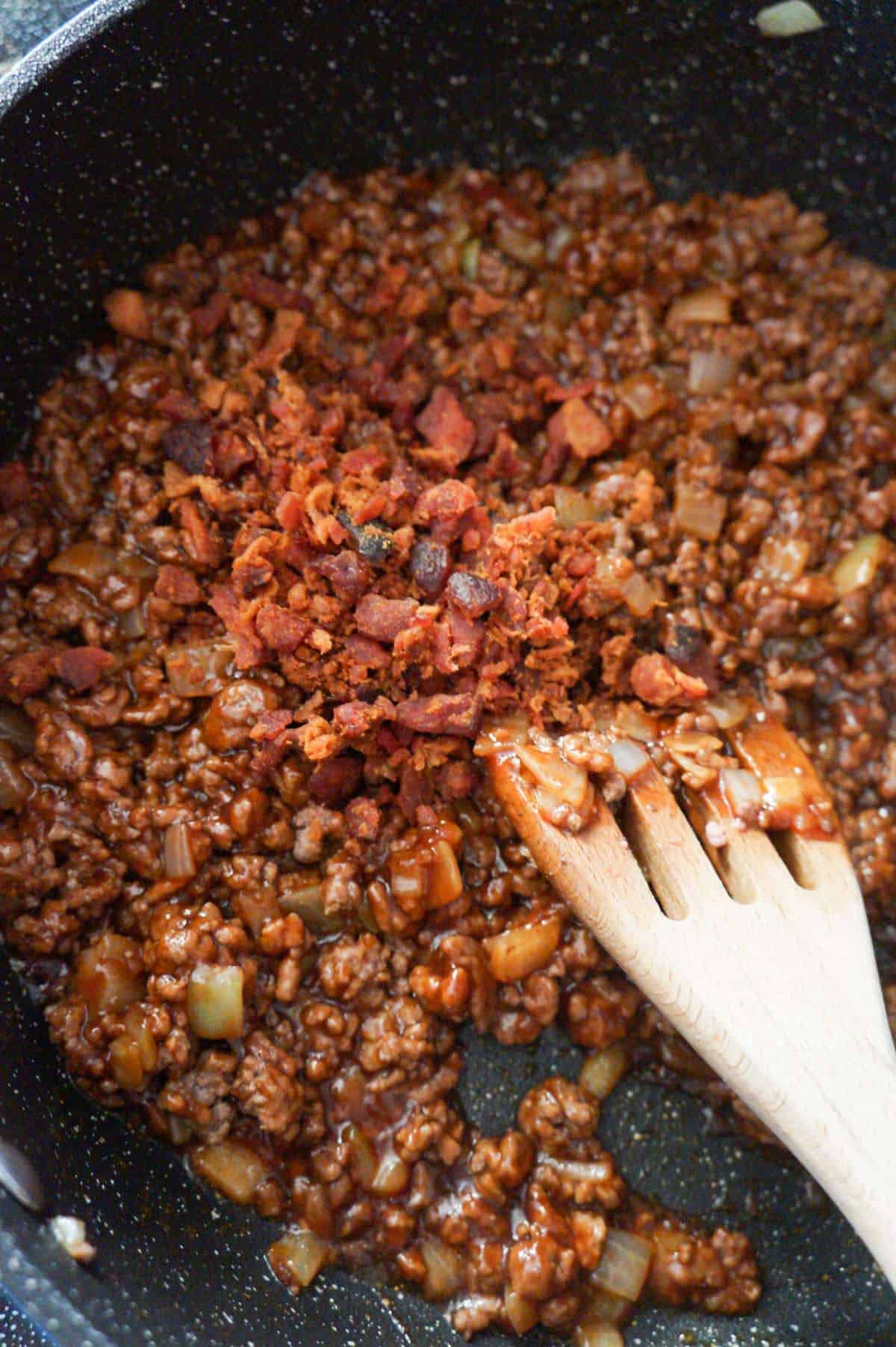 crumbled bacon on top of ground beef tossed in bbq sauce in a saute pan
