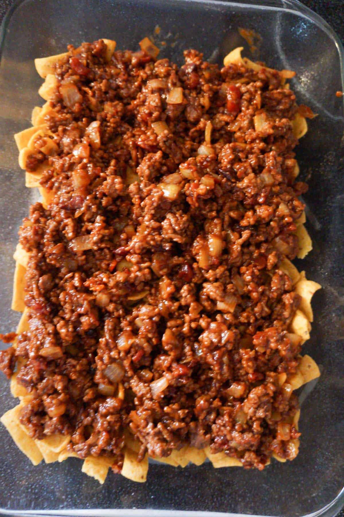 bbq sauce coated ground beef on top of fritos corn chips in a baking dish