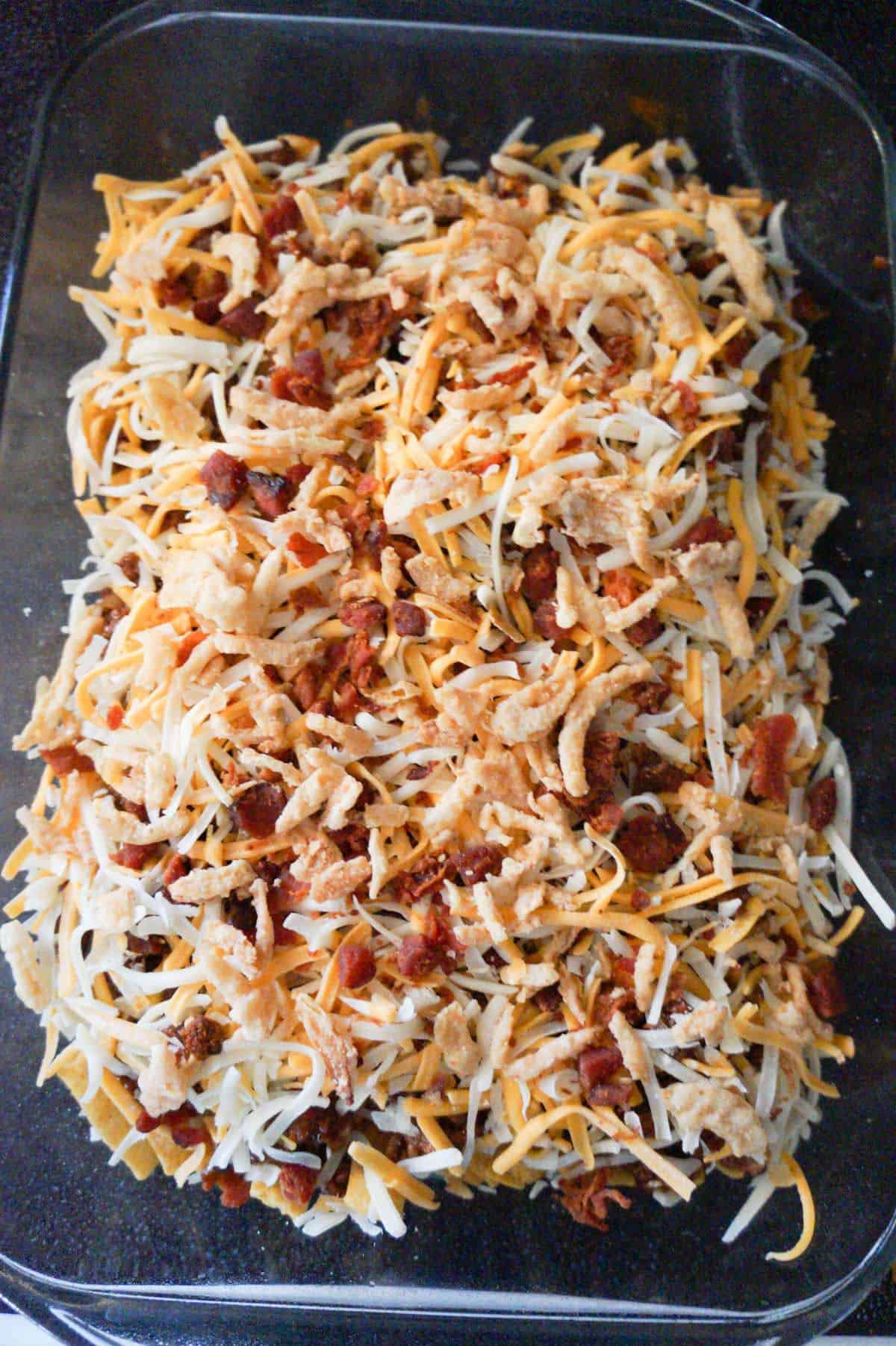 french's fried onions, crumbled bacon and shredded cheese on top of frito pie before baking