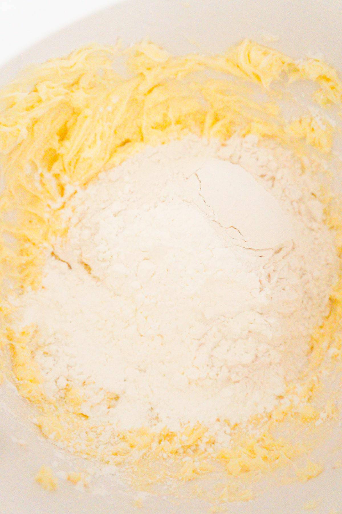corn starch and all purpose flour on top of creamy butter and icing sugar mixture in a mixing bowl