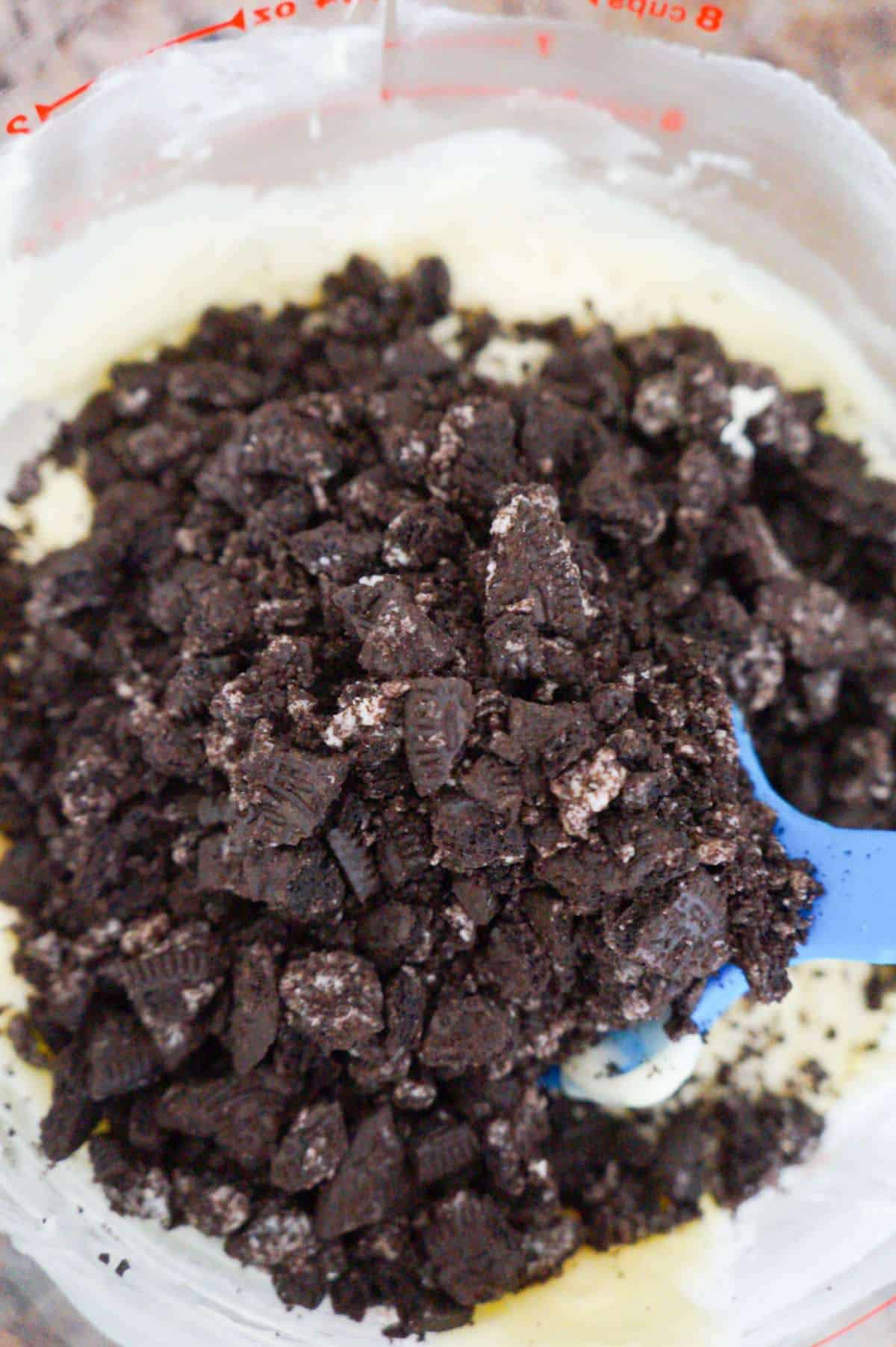 crumbled Oreos on top of melted white chocolate and frosting mixture in a mixing bowl