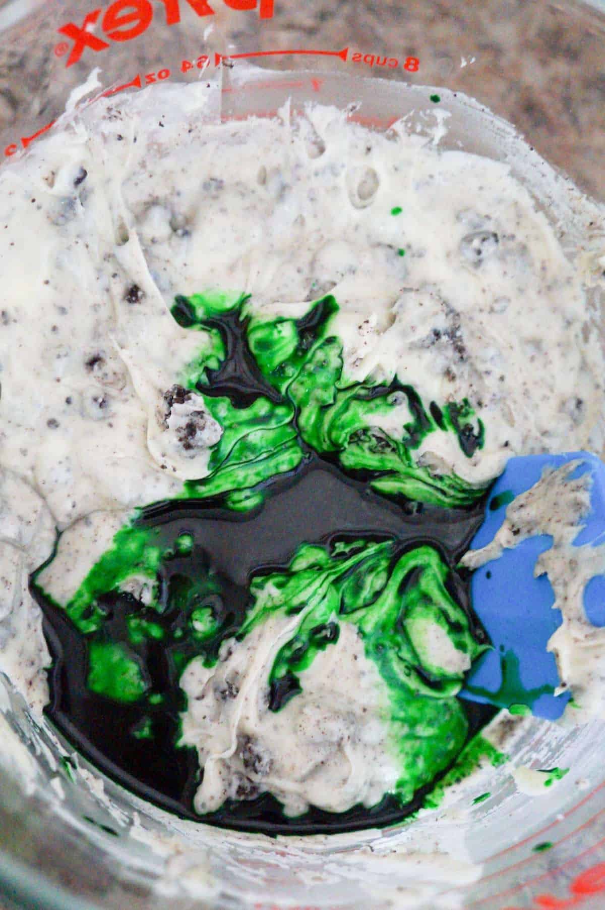green food colouring on top of cookies and cream fudge mixture in a mixing bowl