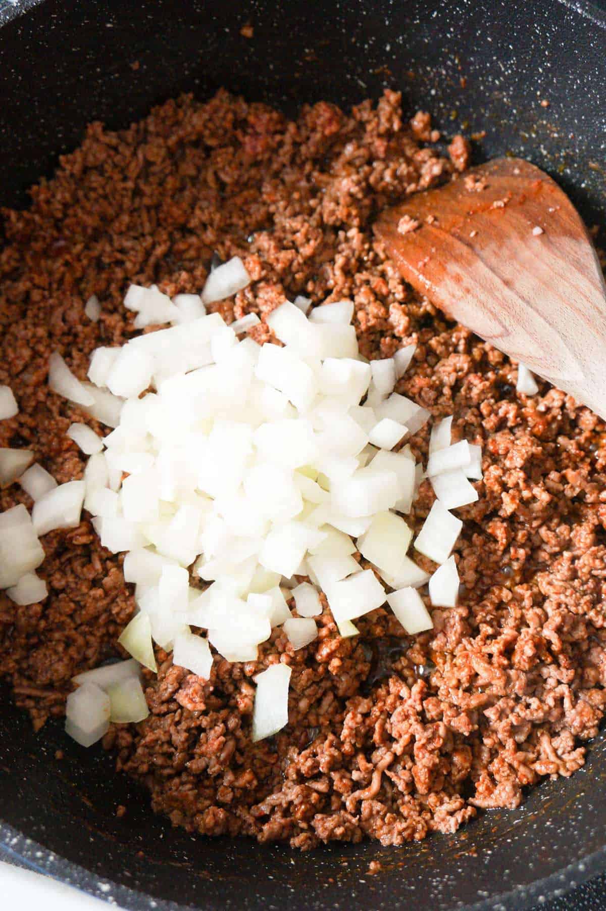 diced onions on top of ground beef in a saute pan